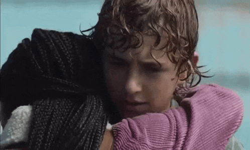a young boy is holding a woman in his arms while standing next to a body of water .