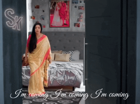 a woman in a yellow saree is standing in a bedroom with a sign that says sk