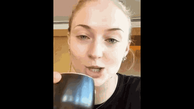 a woman without makeup is drinking from a black mug