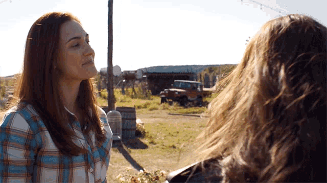 a woman in a plaid shirt is talking to another woman in a field