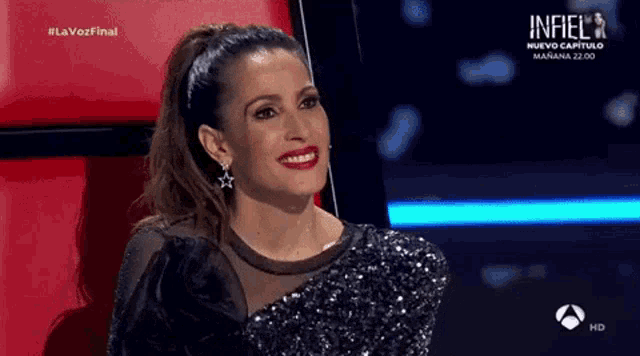 a woman in a black sequined dress is smiling on a television show .