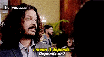 a man with long hair is talking to a woman and says `` i mean it depends . depends on . ''