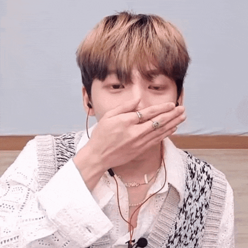 a young man with a ring on his finger covers his mouth