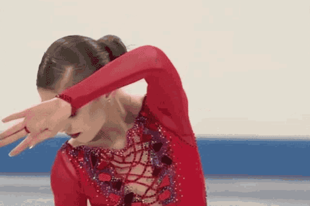 a woman in a red dress is covering her face with her hand while ice skating .