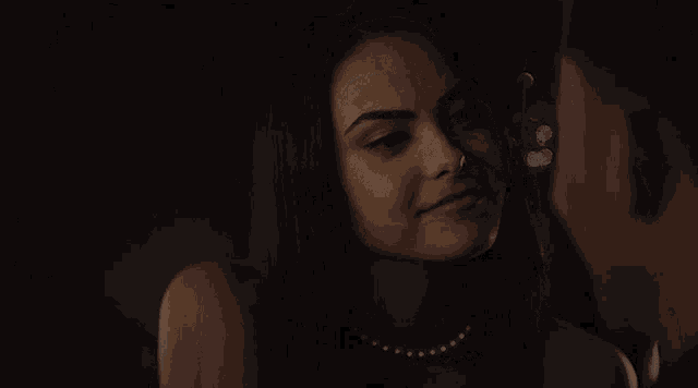 a woman wearing a pearl necklace is looking at a man in a dark room