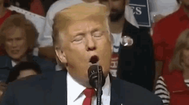 donald trump is yawning while speaking into a microphone at a rally .