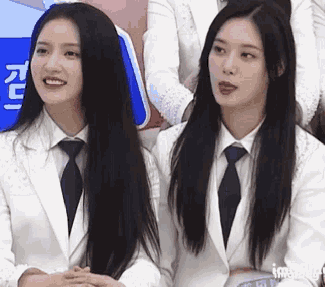 two girls in suits and ties are sitting next to each other and smiling .