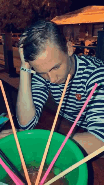 a man wearing a black and white striped shirt with a heart on it looks down at a bowl of straws