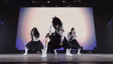 a group of girls are performing on a stage with a large screen behind them that says ' tokyo '