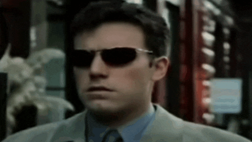 a man wearing sunglasses and a suit looks serious