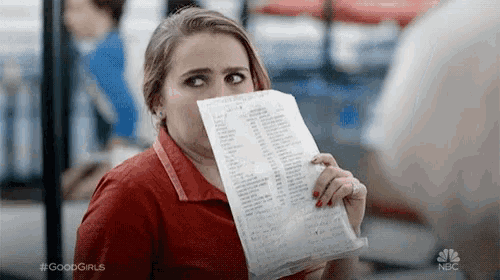 a woman in a red shirt is holding a piece of paper in front of her mouth .