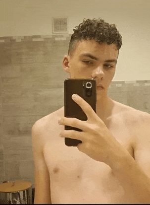 a young man without a shirt is taking a selfie with his cell phone .