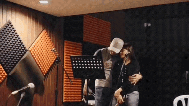 a man and a woman are hugging in a recording studio and the man is wearing a shirt that says ac on it