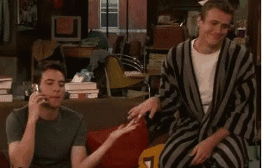 two men are sitting on a couch talking on their cell phones