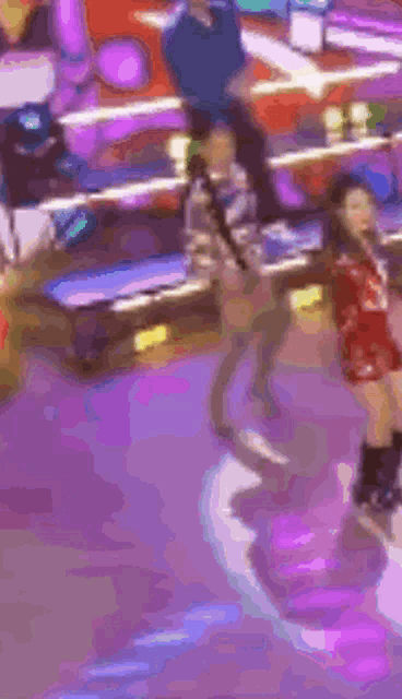 a group of people are dancing on a stage in a room with purple lights .