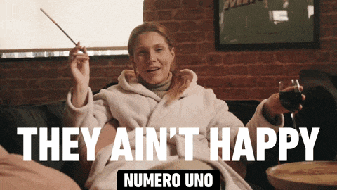 a woman sitting on a couch holding a glass of wine with the words they ain 't happy numero uno above her