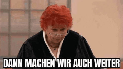 a woman with red hair and glasses is standing in front of a window and says dann machen wir auch weiter .
