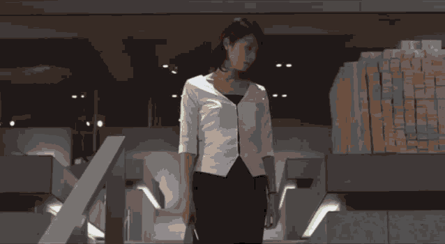 a woman in a white cardigan and black skirt is standing in front of a window .
