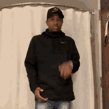 a man wearing a black nike hoodie and a hat is standing in front of a shower curtain