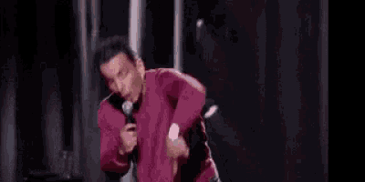 a man in a pink shirt is holding a microphone and talking into it .