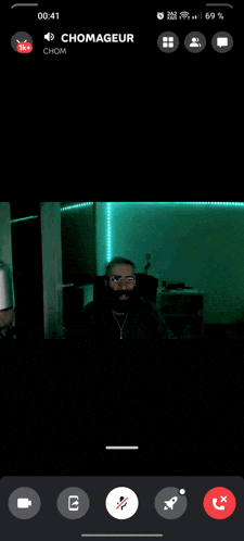 a phone screen shows a man with glasses and a beard and says chomager on the top left