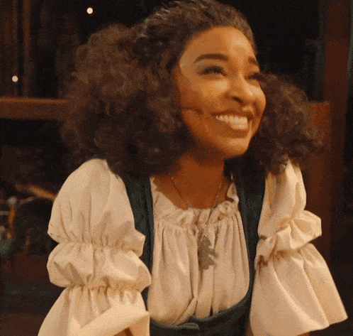 a woman with curly hair is smiling and wearing a green vest and white top