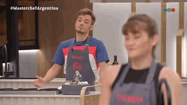 a man wearing an apron that says tomas stands next to a woman