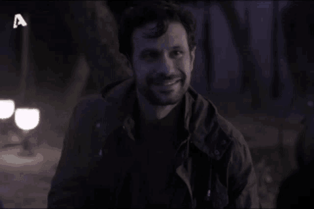 a man with a beard is smiling and the letter a is visible in the corner
