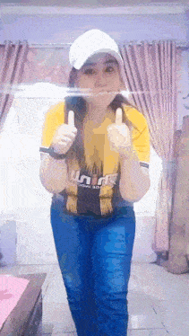 a woman wearing a yellow shirt and a white hat is giving two thumbs up