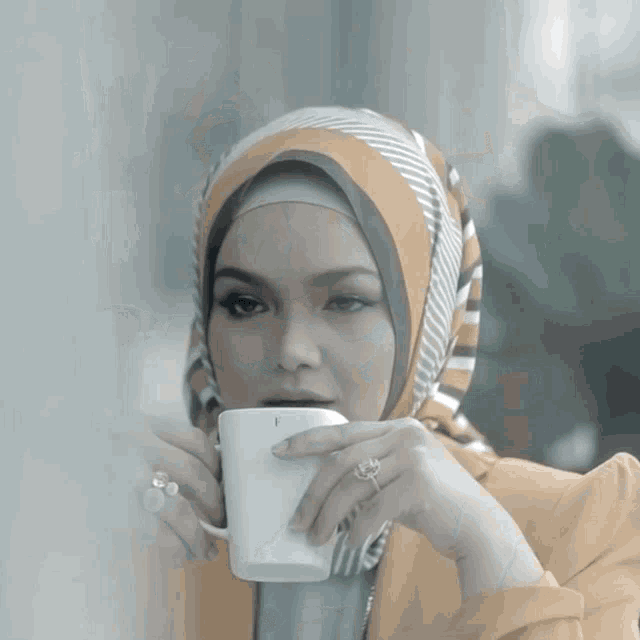 a woman wearing a scarf and a ring is holding a cup with the letter f on it