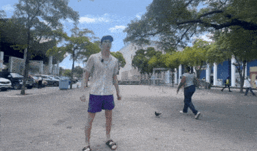 a man in a striped shirt and purple shorts stands on a brick sidewalk in front of a large building