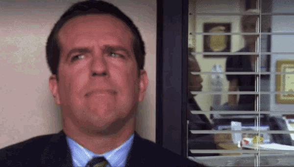 a man in a suit and tie stands in front of a window with blinds