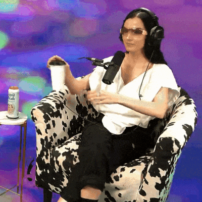 a woman wearing headphones and sunglasses sits in a cow print chair holding a cup and a can of root beer