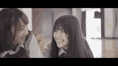 two young girls are standing next to each other in a hallway and smiling .