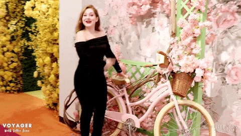 a woman stands in front of a pink bicycle with the words voyager on the bottom right