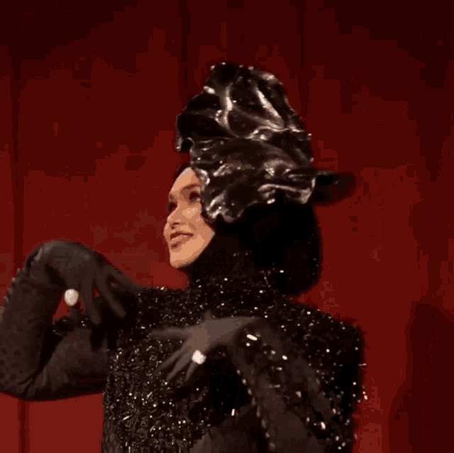 a woman in a black dress and hat is standing on a stage with a red curtain behind her .