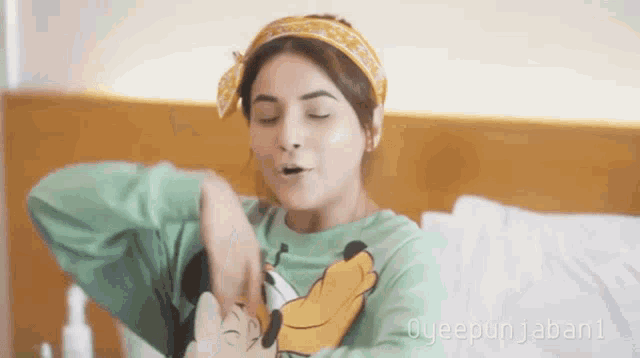 a woman wearing a green shirt with a mickey mouse on it is sitting on a bed with her eyes closed .