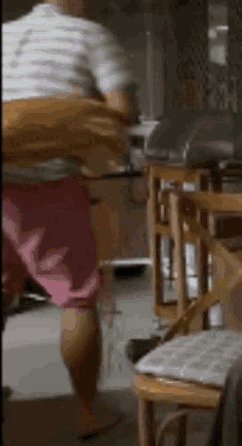 a man in pink shorts is standing in a kitchen next to a table .