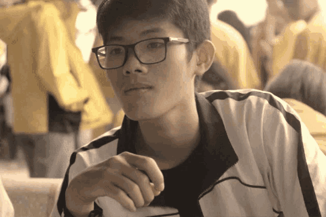 a young man wearing glasses and a white jacket looks at the camera