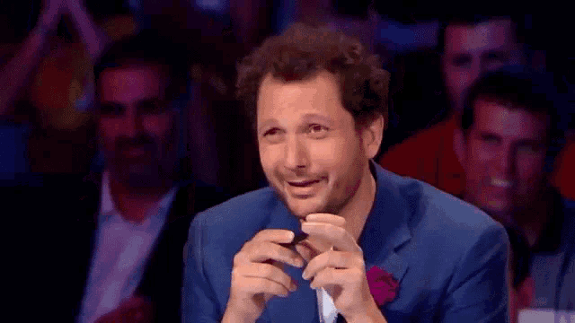 a man in a blue suit is making a funny face while sitting in front of a crowd .
