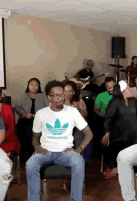 a man in an adidas shirt is sitting in a chair in front of a crowd of people .