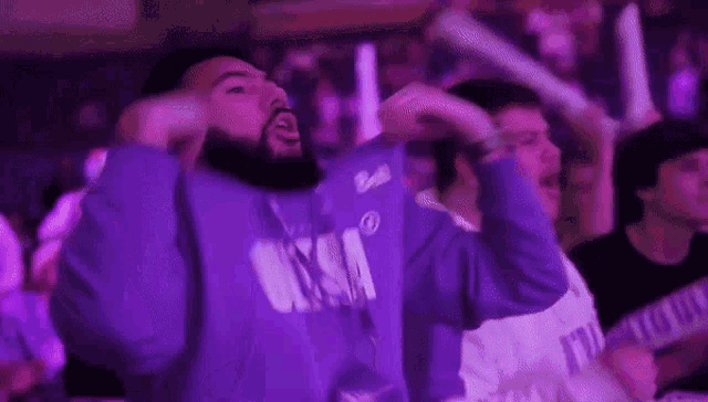 a man wearing a purple shirt with the word bell on it is standing in a crowd of people .