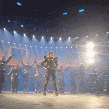 a group of people on roller skates on a stage with a man wearing a costume that says batman