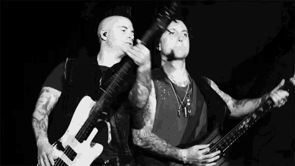 a black and white photo of two men playing guitars .