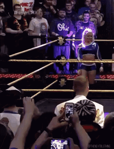 a woman in a blue ohio shirt stands in a wrestling ring surrounded by fans