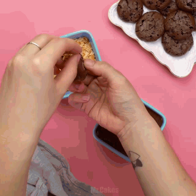 a person with a tattoo on their wrist is putting a cookie into a blue container