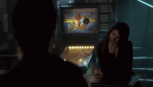 a man and a woman sit at a table in front of a pinball machine that says striped terror on it