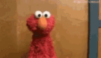 elmo from sesame street is standing in front of a wooden wall and looking at the camera .