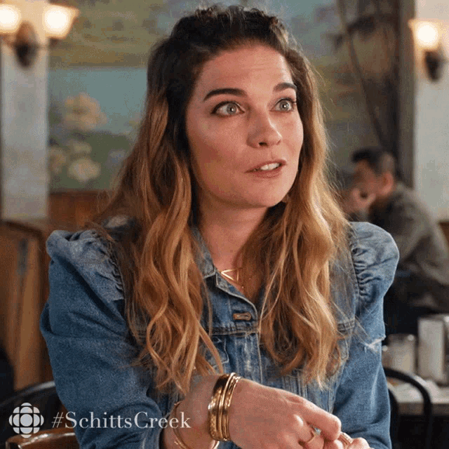 a woman in a denim jacket is sitting at a table with #schitts creek