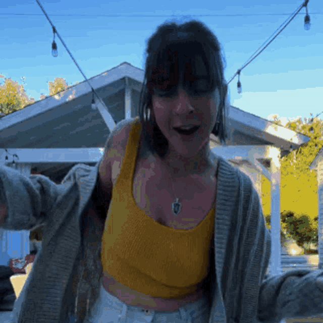 a woman in a yellow tank top and a grey cardigan is dancing